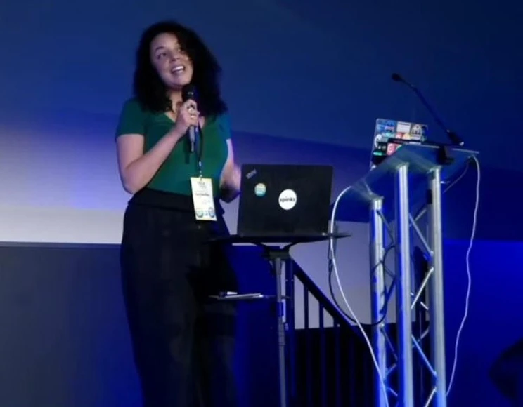A mixed race woman standing with a microphone at a lecturn with a laptop